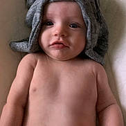 Weston is registered to the contest to win money with this photo: baby, infant, towel, headwear, bare_chest, lying_down, skin, face, eyes, mouth, arm, shoulder, soft_surface, indoor, cute, child, person, newborn, portrait, closeup