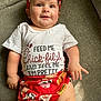 Holly is registered to the contest to win money with this photo: baby, child, smiling, headband, shirt, text, red, white, couch, fabric, clothing, infant, cute, skin, legs, hand, sitting, portrait, indoors, light