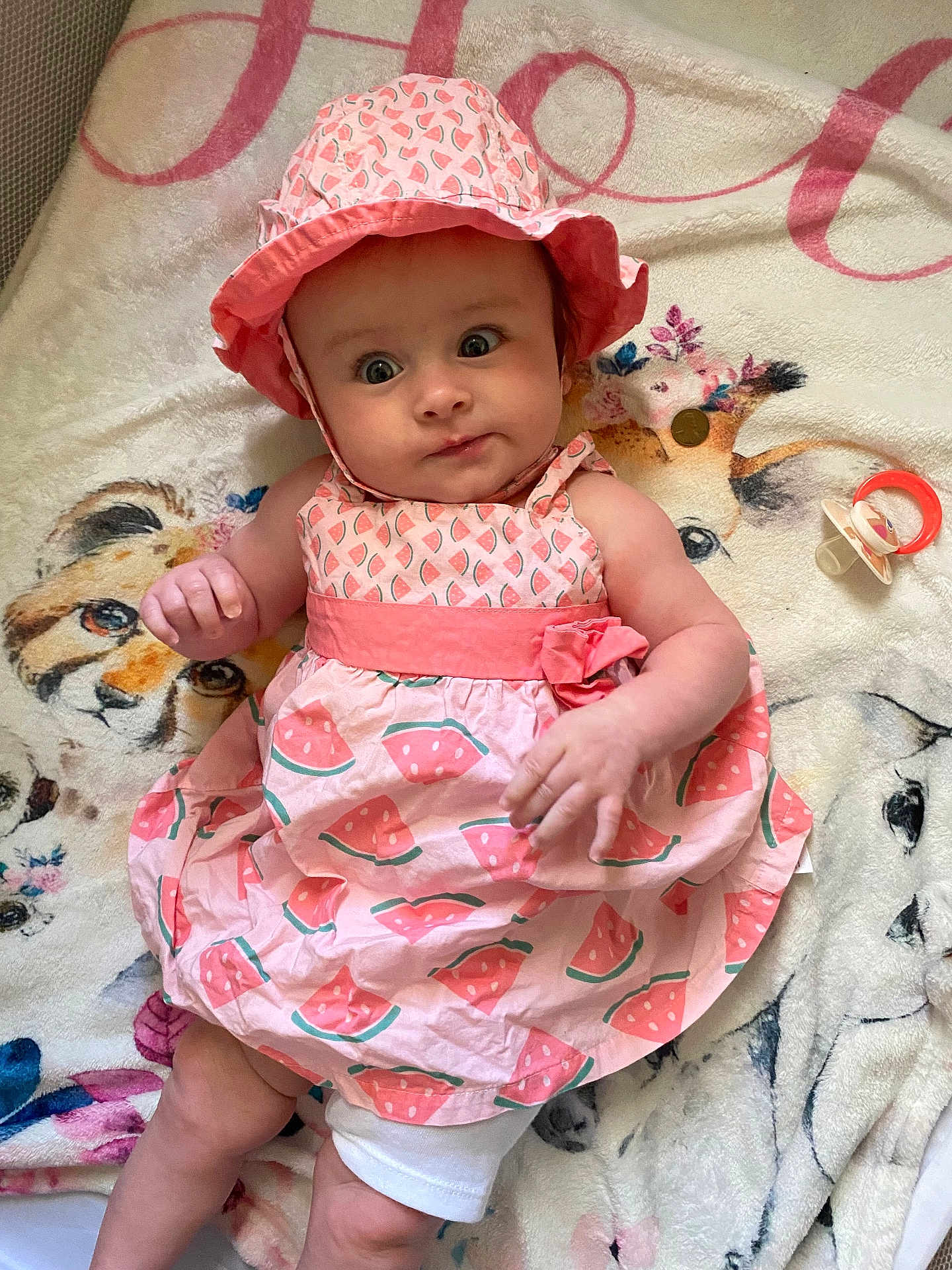 Holly joined the competition — help win amazing prizes! baby, infant, child, pink_dress, hat, watermelon_pattern, blanket, animal_print, pacifier, lying_down, cute, wide_eyes, curious, indoors, soft_texture, adorable, clothing, portrait, person, young_child
