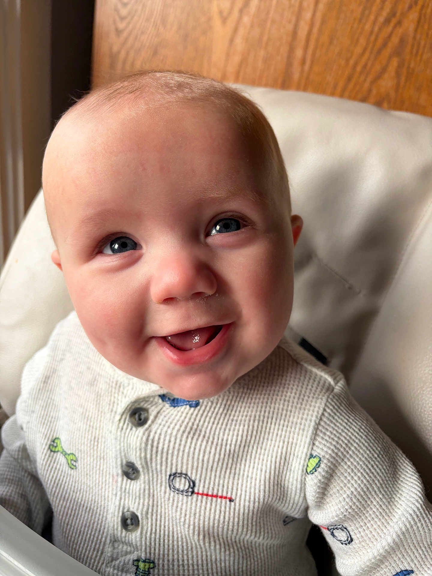 Cohen is registered to the contest to win money with this photo: baby, child, smile, happy, blue_eyes, close_up, onesie, white_clothing, indoor, infant, face, cute, joyful, sitting, wooden_background, soft_light, portrait, childhood, young, person