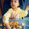 child, toddler, baby, high_chair, cereal, banana, raisins, breakfast, food, eating, sitting, indoor, portrait, yellow_shirt, hoodie, smiling, wide_eyed, messy_tray, home, daylight
