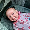 baby, infant, smiling, pink_onesie, bows, pacifier, grey_carrier, cushion, cute, face, head, happy, child, person, apparel, fabric, seat, portrait, newborn, comfort