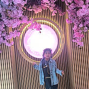 Muqadas joined the competition — help win amazing prizes! child, girl, denim_jacket, necklaces, pink_flowers, blossoms, wooden_wall, vertical_slats, glowing_sign, indoor, floor, fashion, portrait, standing, casual_clothing, boots, lighting, decor, young_person, curly_hair