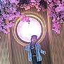 child, girl, denim_jacket, necklaces, pink_flowers, blossoms, wooden_wall, vertical_slats, glowing_sign, indoor, floor, fashion, portrait, standing, casual_clothing, boots, lighting, decor, young_person, curly_hair