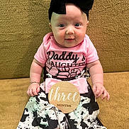 Juniper joined the competition — help win amazing prizes! baby, infant, child, girl, headband, bow, pink_shirt, daddys_daughter, cow_print_pants, white_socks, wooden_sign, three_months, couch, golden_background, sitting, cute, portrait, happy, indoors, person