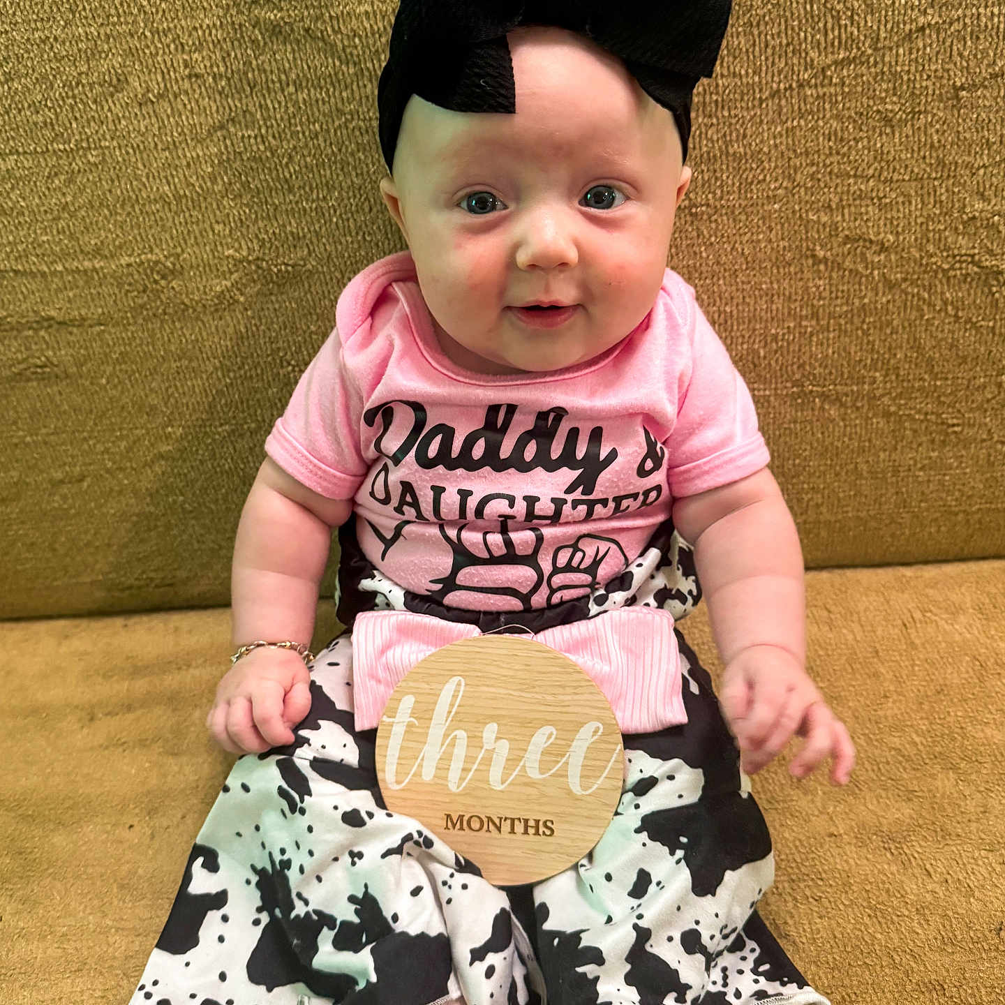 Juniper joined the competition — help win amazing prizes! baby, infant, child, girl, headband, bow, pink_shirt, daddys_daughter, cow_print_pants, white_socks, wooden_sign, three_months, couch, golden_background, sitting, cute, portrait, happy, indoors, person