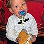 toddler, child, pacifier, white_shirt, black_bow_tie, curly_hair, orange_cloth, tags, couch, patterned_couch, indoor, sitting, cute, holding, clothing, person, face, baby, adorable, young_child