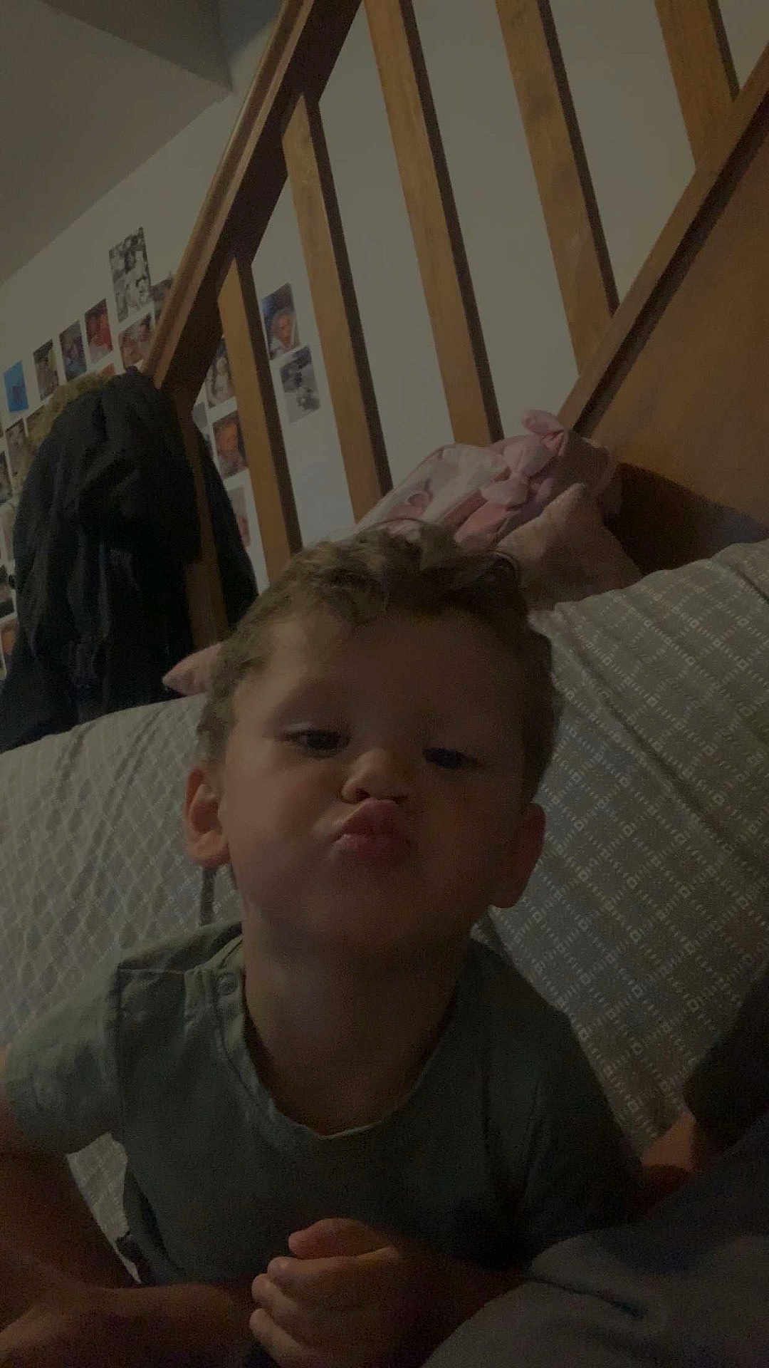 Lyann a rejoint le concours — aidez-le/la à gagner de superbes lots ! child, puckered_lips, bed, wooden_headboard, photos, wall, indoor, young_child, curly_hair, green_shirt, pillow, blanket, hand, face, person, portrait, casual, home, furniture, sleep_area