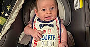 Gunner is registered to the contest to win money with this photo: baby, car_seat, bib, smiling, infant, clothing, blanket, seatbelt, indoor, cute, child, face, person, sitting, celebration, holiday, red, white, blue, patriotic