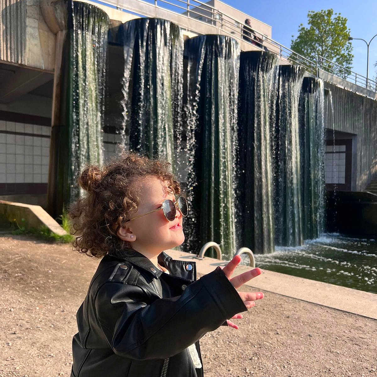 Elen Elabed participe au concours pour gagner de l'argent avec cette photo : child, curly_hair, sunglasses, leather_jacket, waterfall, outdoor, sunny, pose, water, nature, person, daylight, river, rock, casual_clothing, cool, young, park, reflection, fashion