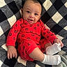 baby, infant, smile, red_clothing, spiderman_pattern, white_socks, blanket, checkered_pattern, cozy, happy, cute, child, lying_down, portrait, indoors, soft_texture, face, small_hand, footwear, warm