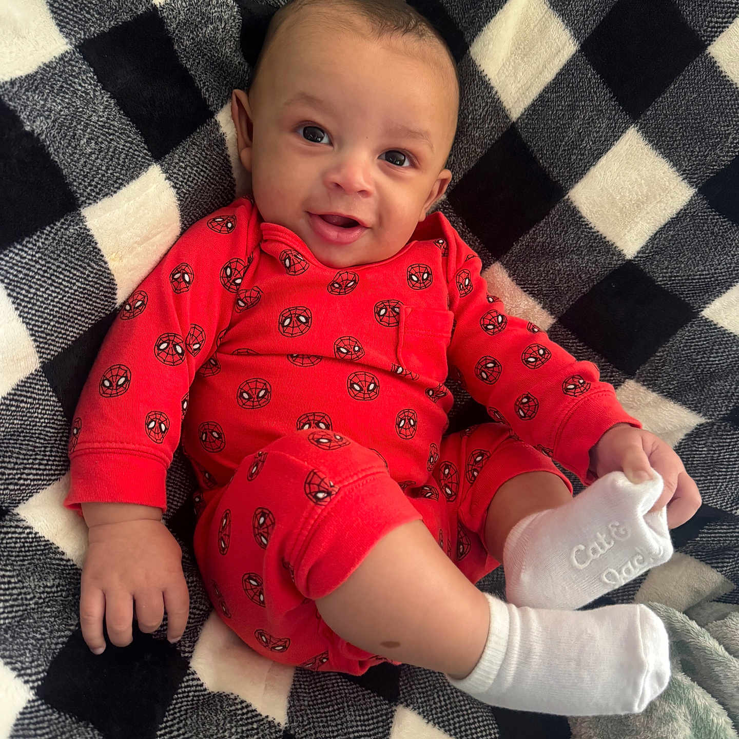 Karsyn joined the competition — help win amazing prizes! baby, infant, smile, red_clothing, spiderman_pattern, white_socks, blanket, checkered_pattern, cozy, happy, cute, child, lying_down, portrait, indoors, soft_texture, face, small_hand, footwear, warm