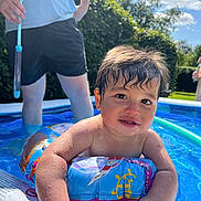 Austin is registered to the contest to win money with this photo: toddler, child, pool, water, floatie, summer, outdoor, sunny, blue_sky, clouds, person, water_droplets, toy, adult, greenery, playing, fun, vacation, relaxing, daytime