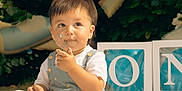 Austin is registered to the contest to win money with this photo: toddler, child, cake, face_paint, messy, celebration, balloon, outdoor, greenery, blocks, letters, clothing, white_shirt, overalls, portrait, happy, party, cute, baby, food