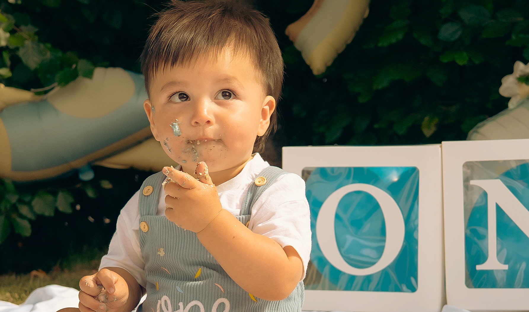 Austin is registered to the contest to win money with this photo: toddler, child, cake, face_paint, messy, celebration, balloon, outdoor, greenery, blocks, letters, clothing, white_shirt, overalls, portrait, happy, party, cute, baby, food