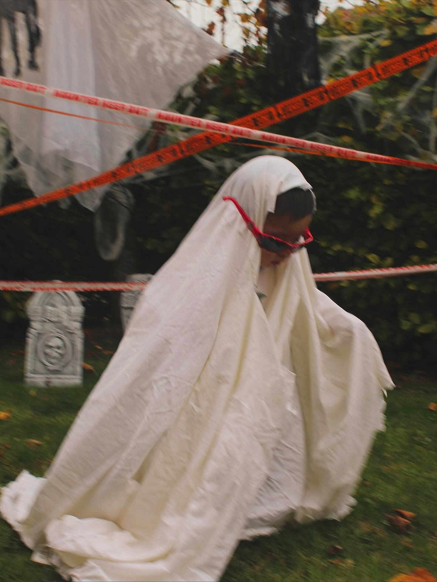 Austin joined the competition — help win amazing prizes! child, ghost_costume, white_sheet, red_sunglasses, halloween, outdoor, garden, grass, halloween_decorations, caution_tape, spooky, fun, costume, holiday, seasonal, playful, person, face, head, greenery