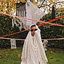 child, costume, ghost, sunglasses, halloween, yard, grass, fall_leaves, decoration, tombstone, caution_tape, spooky, outdoor, tree, shrubbery, holiday, fun, playful, white_sheet, face