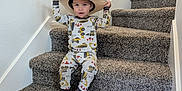 Aiden is registered to the contest to win money with this photo: toddler, child, stairs, carpet, hat, cowboy_hat, pajamas, barefoot, indoor, smiling, young_child, person, home, wall, railing, footwear, sitting, cute, playful, casual