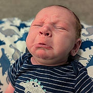 Bryson is registered to the contest to win money with this photo: baby, infant, face, expression, frown, clothing, onesie, striped, dinosaur, blanket, pattern, cute, child, newborn, portrait, skin, head, person, lying, indoor