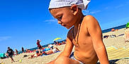 Saymon participe au concours pour gagner de l'argent avec cette photo : child, beach, sand, sunlight, headscarf, swim_trunks, summer, sea, sky, people, vacation, outdoor, relaxation, sunshine, holiday, shore, playful, casual, portrait, sunbathing