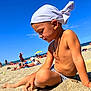 child, beach, sand, sunlight, headscarf, swim_trunks, summer, sea, sky, people, vacation, outdoor, relaxation, sunshine, holiday, shore, playful, casual, portrait, sunbathing