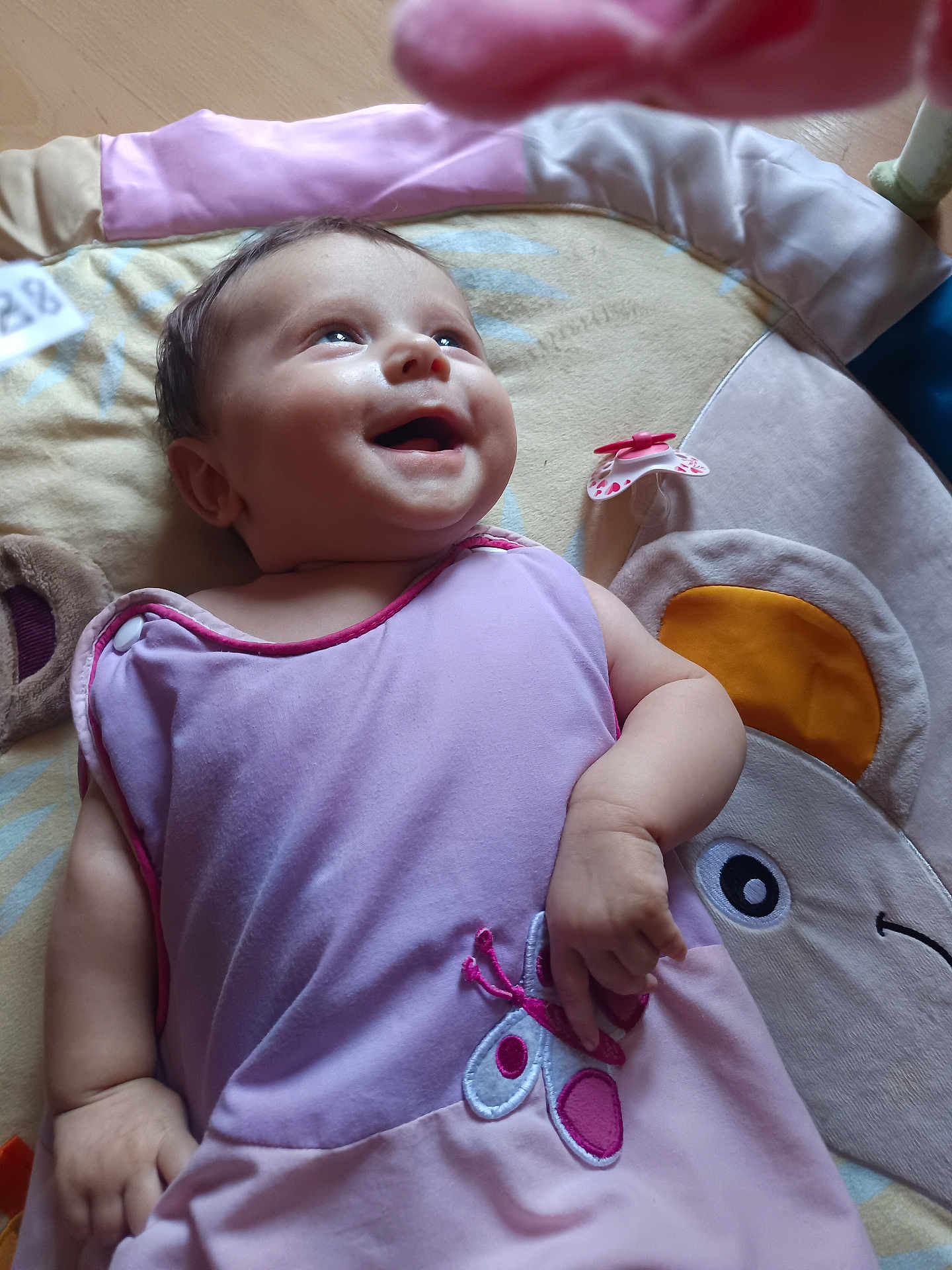 Shelly participe au concours pour gagner de l'argent avec cette photo : arm, baby, child, closeup, cute, expression, face, floor, hand, happy, indoor, infant, lying_down, person, play_mat, purple_dress, skin, smiling, soft_toy, toy