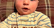 Julius joined the competition — help win amazing prizes! baby, infant, child, face, blue_eyes, plaid, cushion, clothing, onesie, striped, hands, rosy_cheeks, portrait, indoor, cute, young, person, cozy, closeup, expression