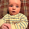 baby, infant, child, face, blue_eyes, plaid, cushion, clothing, onesie, striped, hands, rosy_cheeks, portrait, indoor, cute, young, person, cozy, closeup, expression