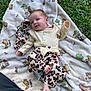 baby, blanket, outdoor, grass, infant, clothing, pattern, headband, cute, lying_down, teddy_bear_pattern, nature, child, soft_texture, foot, hand, smile, person, apparel, relaxing
