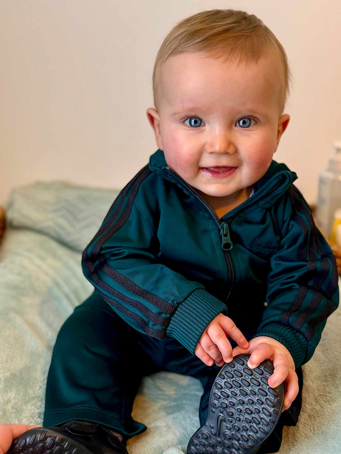 Noah a rejoint le concours — aidez-le/la à gagner de superbes lots ! baby, child, blue_eyes, smiling, tracksuit, sitting, shoe, hand, face, indoor, blanket, curly_hair, happy, cute, portrait, young_child, clothing, footwear, person, infant