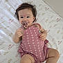 baby, infant, pacifier, pink_romper, crown_pattern, crib_mattress, little_princess_text, child, cute, smiling, lying_down, indoors, soft_lighting, toddler, hand, foot, hair, skin, clothing, playful