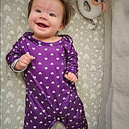 Camila joined the competition — help win amazing prizes! baby, smiling, purple_onesie, heart_pattern, lying_down, plush_toy, bear_toy, crib, mattress, infant, cute, happy, child, clothing, indoors, portrait, face, hands, baby_girl, sleepwear