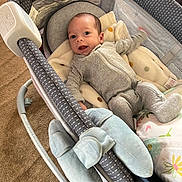 Angel joined the competition — help win amazing prizes! baby, infant, smile, onesie, blanket, plush_toy, baby_rocker, carpet, happy, indoor, child, face, head, person, soft_toy, footwear, clothing, comfort, cute, lying_down