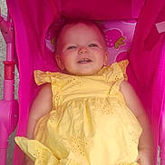Charlotte is registered to the contest to win money with this photo: baby, child, yellow_dress, pink_stroller, smile, happy, infant, outdoor, seat, toy, cute, person, sunlight, cheerful, baby_clothing, strawberry_pattern, baby_toy, relaxing, portrait, playful