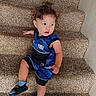 blue_clothing, carpet, casual, child, curious, curly_hair, cute, footwear, home, indoor, looking_away, nba, person, portrait, sandals, sitting, socks, stairs, toddler, young_child