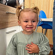 Lyna participe au concours pour gagner de l'argent avec cette photo : blue_chair, child, clothing, cute, dress, earrings, furniture, green_dress, hand, happy, home, indoor, necklace, person, pigtails, portrait, smile, toddler, wooden_cabinet, young_child