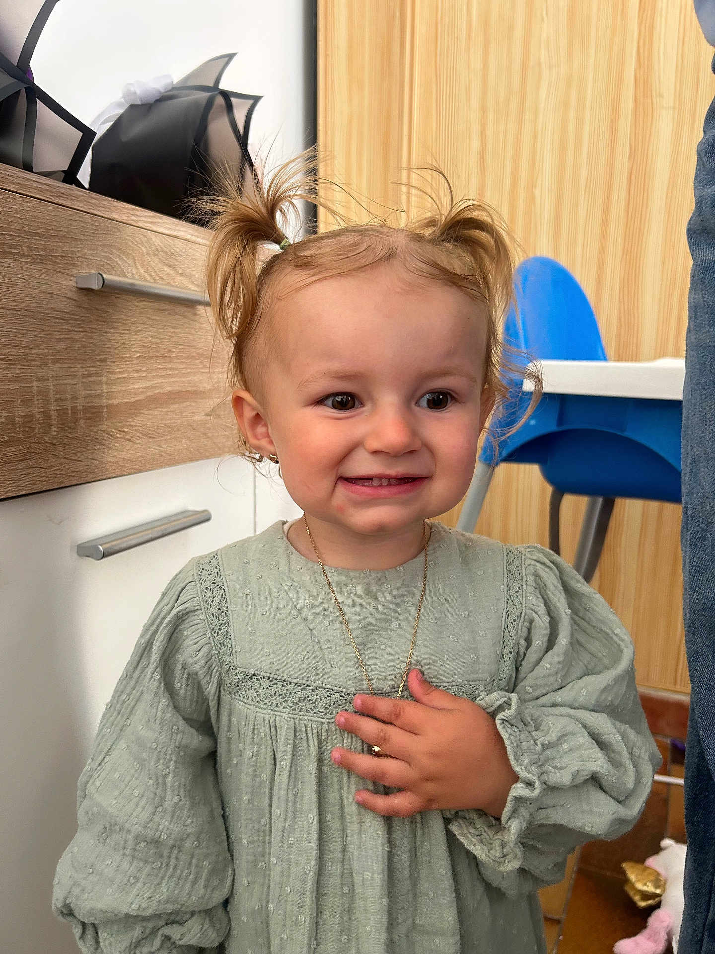 Lyna participe au concours pour gagner de l'argent avec cette photo : blue_chair, child, clothing, cute, dress, earrings, furniture, green_dress, hand, happy, home, indoor, necklace, person, pigtails, portrait, smile, toddler, wooden_cabinet, young_child