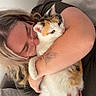 person, cat, calico_cat, glasses, tattoo, butterfly_tattoo, hugging, indoor, couch, affection, pet, animal, love, casual_clothing, light_hair, closeup, comfort, relaxation, home, furniture