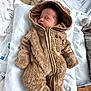 baby, newborn, infant, sleeping, hooded_suit, fuzzy_suit, onesie, zipper, pillow, bed, hospital_bed, blanket, cozy, soft_texture, portrait, closed_eyes, peaceful_expression, lying_down, mittens, cute