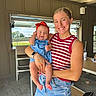 Hadley is registered to the contest to win money with this photo: baby, child, woman, smile, indoor, casual_clothing, denim_shorts, headband, holding, portrait, happy, person, young_adult, striped_shirt, accessory, window, daylight, floor, chair, table