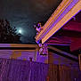 cat, tuxedo_cat, moon, night_sky, gutter, roof, fence, lantern, purple_light, orange_light, tree_silhouette, house, porch, outdoor, pet, wooden_fence, illumination, clouds, evening, balcony