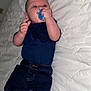 Tyree is registered to the contest to win money with this photo: baby, infant, pacifier, clothing, denim_shorts, blue_shirt, sneakers, footwear, lying_down, bed, quilt, blanket, cute, child, person, indoors, young_child, small_hands, face, eyes