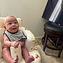 baby, infant, bib, inflatable_seat, dinosaur_pattern, striped_clothing, smiling, curious, indoor, floor, television, furniture, carpet, wall, seat, child, person, happy, cute, home