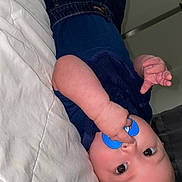 Tyree is registered to the contest to win money with this photo: baby, pacifier, infant, lying_down, blue_clothing, white_bedspread, hand, face, cute, indoors, skin, child, young, sleepwear, bed, expression, person, portrait, chubby, resting
