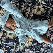 David is registered to the contest to win money with this photo: baby, infant, child, robe, hooded_clothing, blanket, floral_pattern, socks, lying_down, cute, playful, indoor, soft_texture, curious, small_hands, small_feet, portrait, cozy, comfortable, fabric