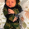 Jensen is registered to the contest to win money with this photo: newborn, baby, sleeping, camouflage_clothing, hoodie, pants, cushion, floral_pattern, infant, peaceful, cute, indoors, portrait, child, resting, small_hands, face, closed_eyes, cozy, soft_lighting