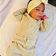 Valerie is registered to the contest to win money with this photo: baby, infant, child, headband, flower, pajamas, ribbed_clothing, beige, blanket, soft, lying_down, curious_expression, indoors, cute, small_hands, face, person, cozy, newborn, resting
