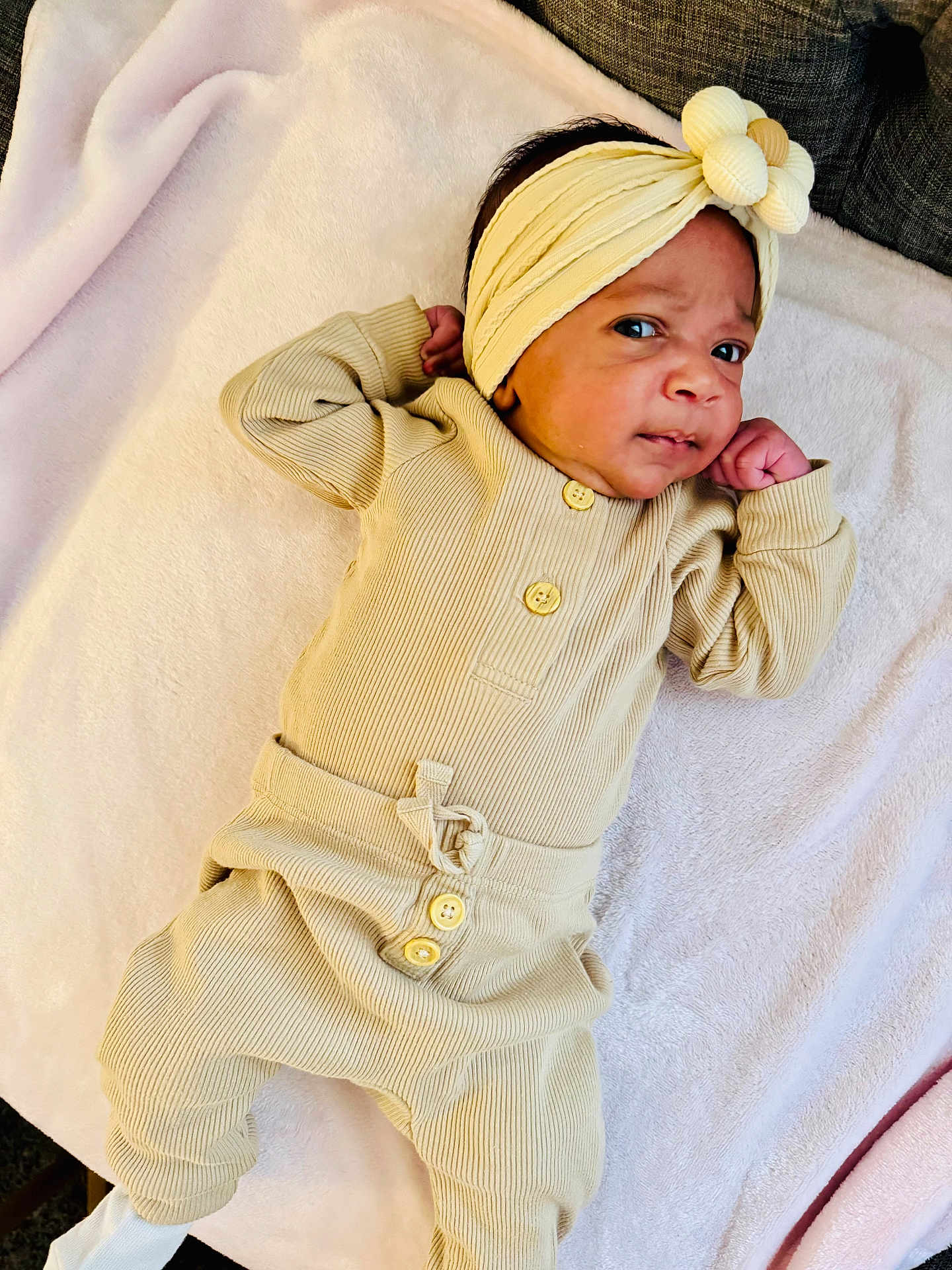 Valerie is registered to the contest to win money with this photo: baby, infant, child, headband, flower, pajamas, ribbed_clothing, beige, blanket, soft, lying_down, curious_expression, indoors, cute, small_hands, face, person, cozy, newborn, resting