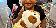Jiayze is registered to the contest to win money with this photo: toddler, child, smiling, shopping_cart, plush_toy, store, indoor, person, curly_hair, clothing, red_shorts, black_shirt, toy, retail, poster, stitch, happy, holding, footwear, five_below