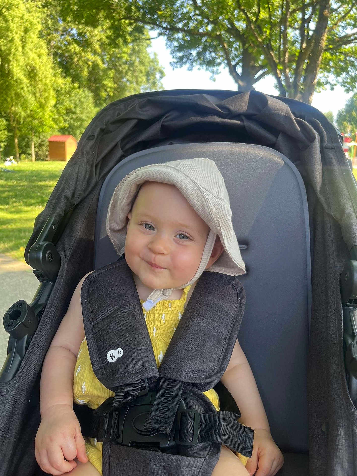 Jade participe au concours pour gagner de l'argent avec cette photo : baby, child, stroller, hat, yellow_outfit, smile, outdoor, sunny, trees, greenery, park, seatbelt, infant, cute, face, person, headwear, happy, nature, daylight